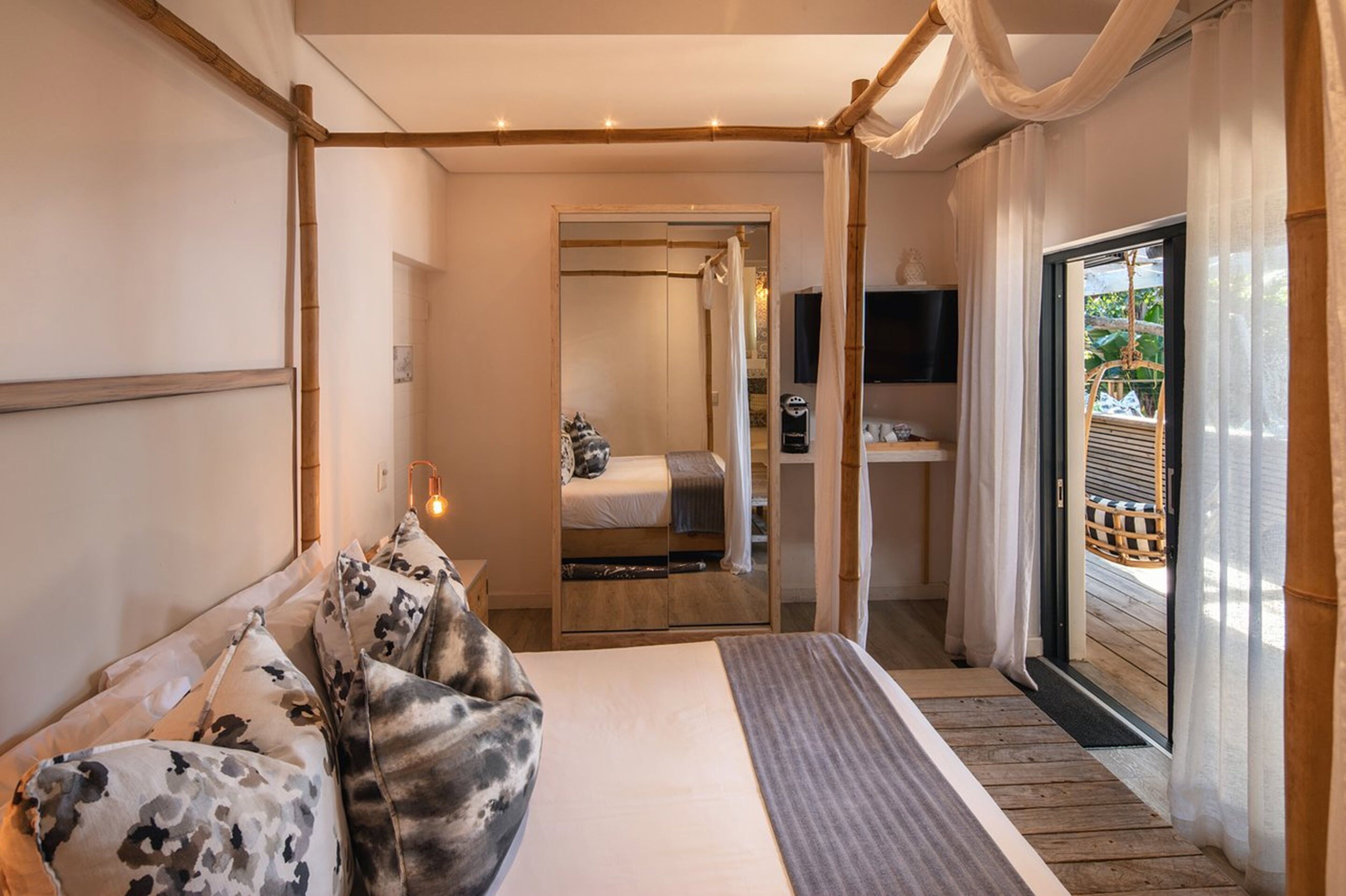 A bedroom with a bed, a bedside table, a mirror, a wardrobe, and a sliding glass door leading to an outdoor area.