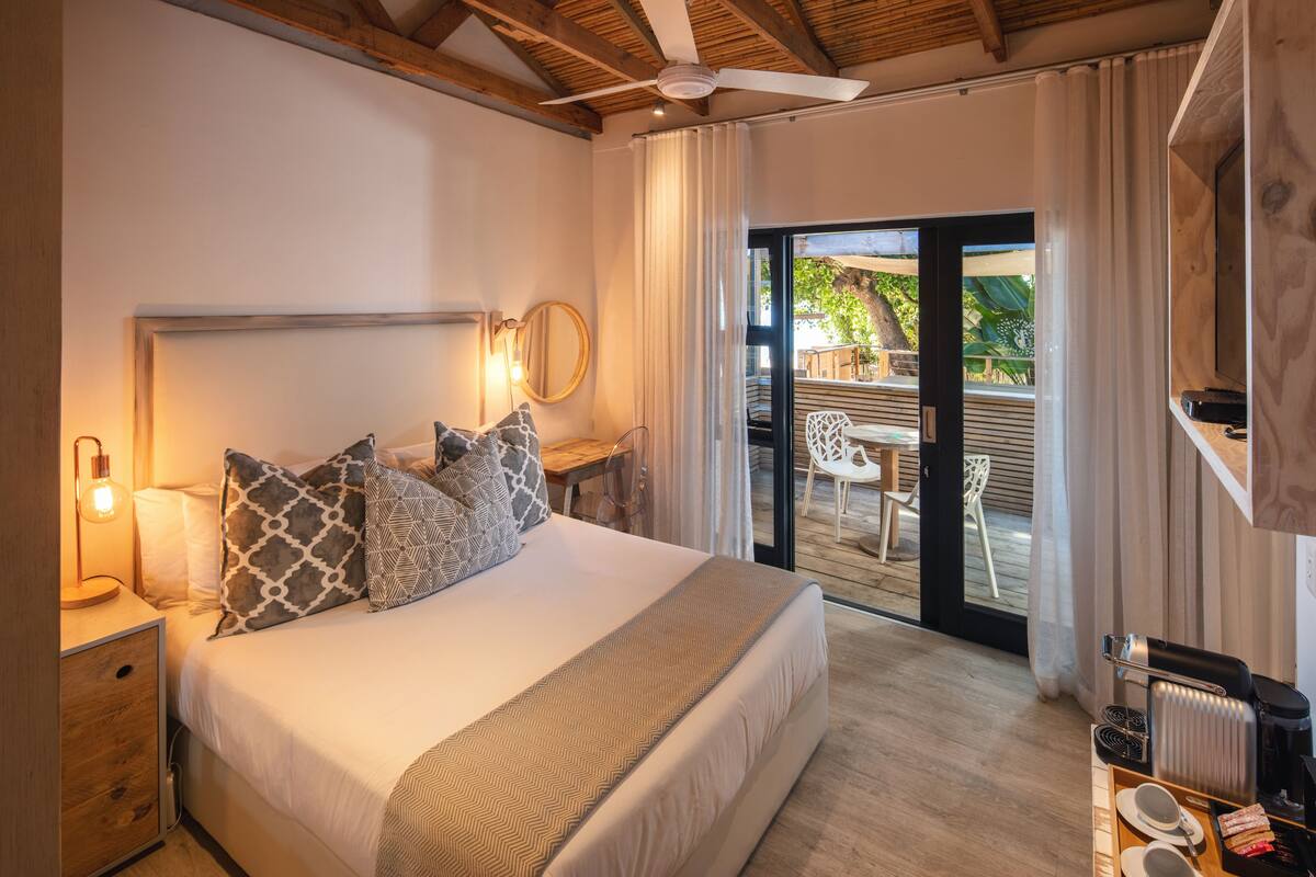 Quarto com cama grande, abajures, espelho e vista para um pátio externo.