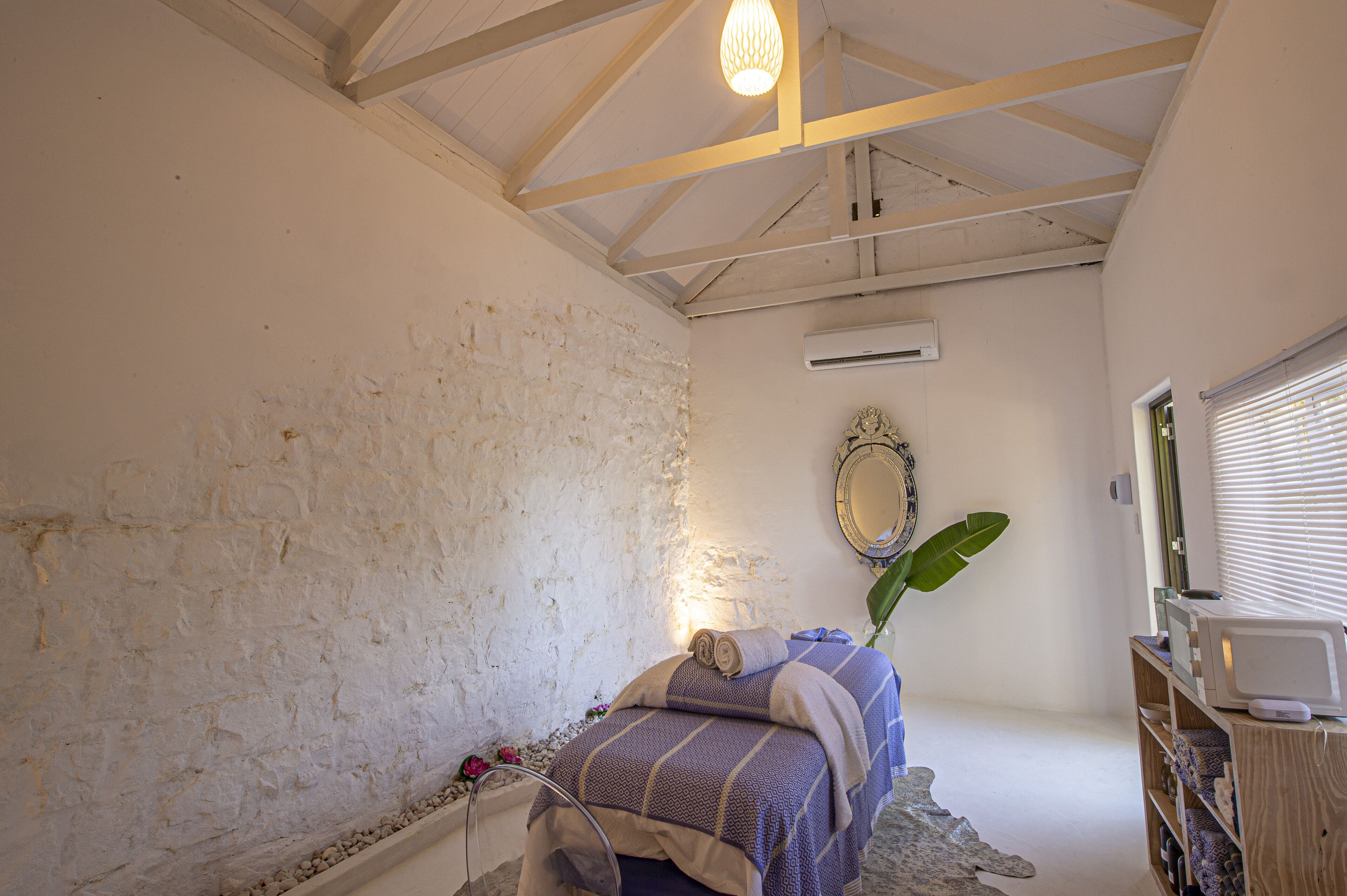 A bedroom with a bed, a wooden ceiling, an air conditioning unit, a mirror, and a window with blinds.