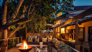 An outdoor seating area with a fire pit, cushions, and wooden furniture. - The Bungalow  (Plettenberg Bay)
