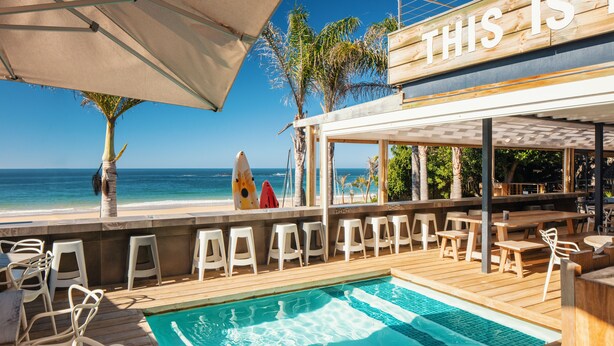 A poolside area with a view of the ocean, wooden deck, and bar seating. - The Bungalow  (Plettenberg Bay)