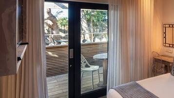 Une chambre d’hôtel comprenant un lit, un bureau avec un ordinateur, une chaise et donnant sur un espace extérieur aménagé avec une table et des chaises.