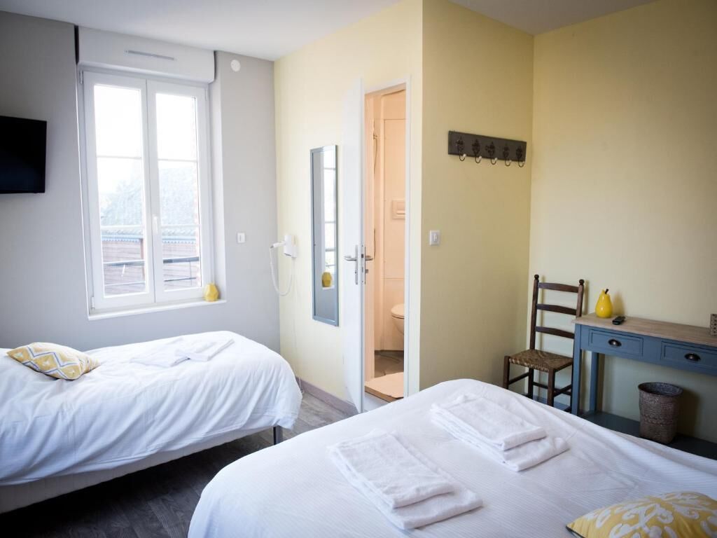 Quarto de hotel com duas camas, uma escrivaninha, uma cadeira, uma televisão e a porta do banheiro.