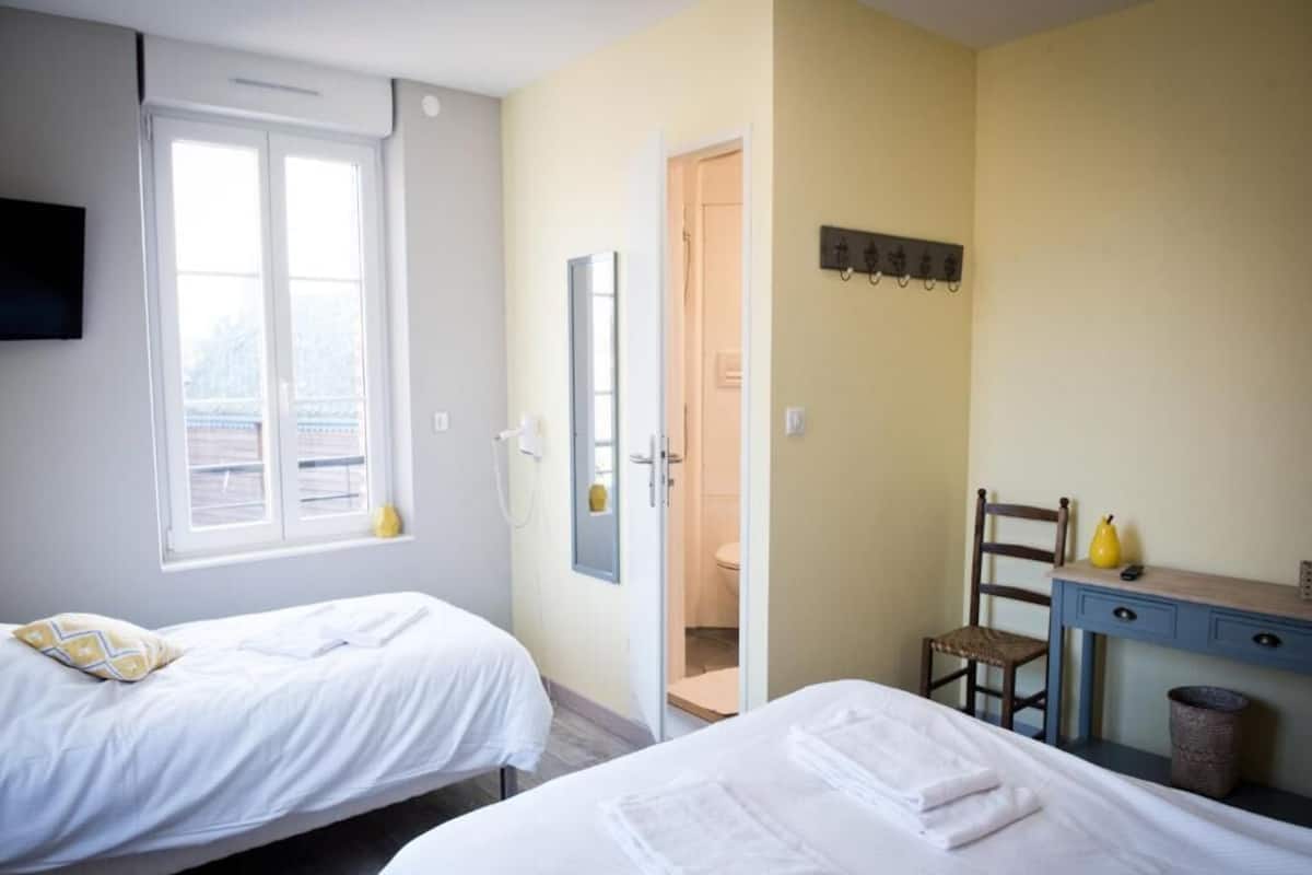 Quarto de hotel com duas camas, uma escrivaninha, uma cadeira, uma televisão e a porta do banheiro.