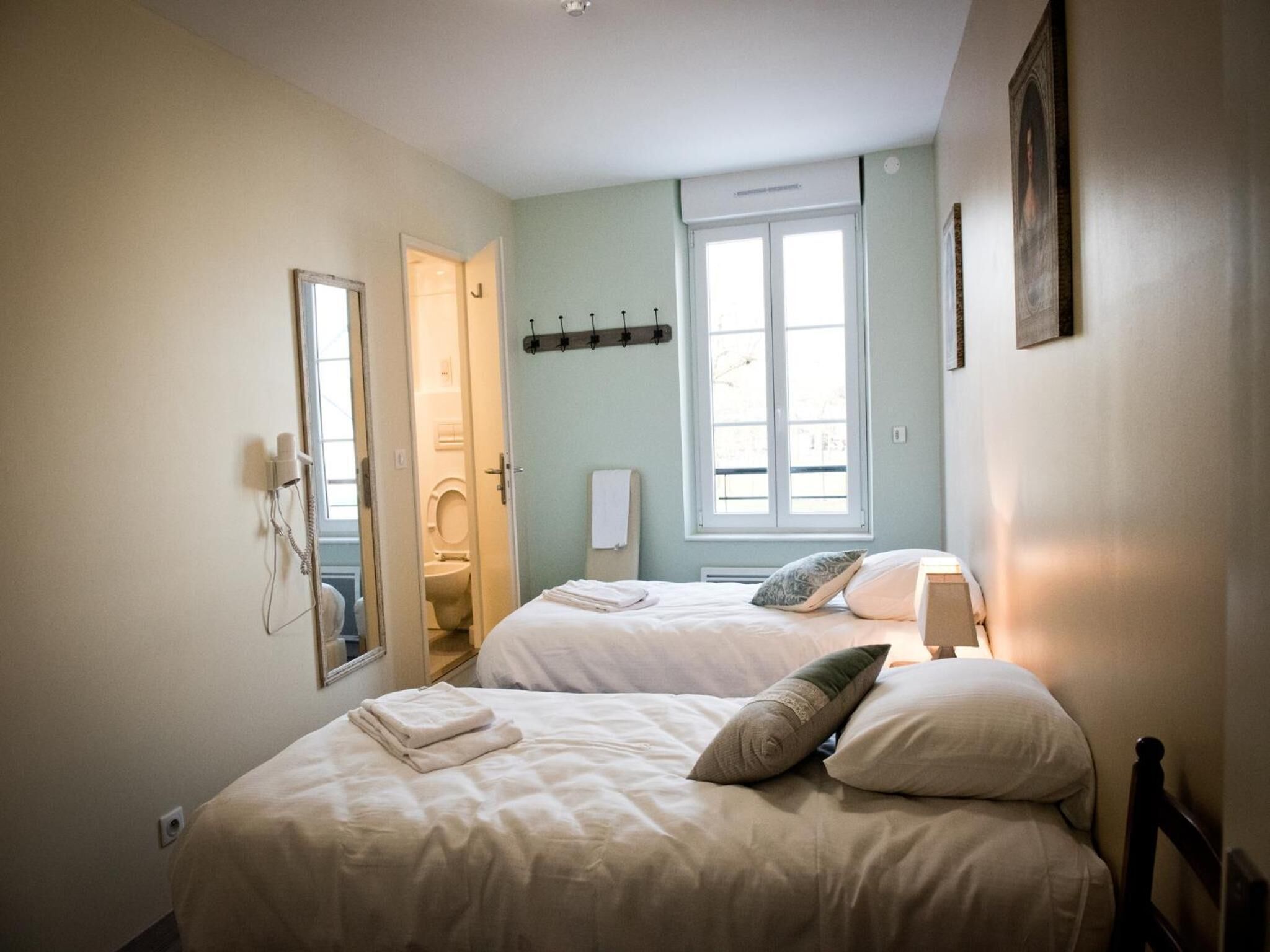 A bedroom with two beds, a window, a mirror, and a door leading to a bathroom.