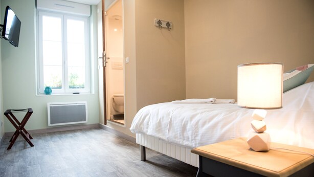 Habitación de hotel con cama, mesita de noche, lámpara, televisor, ventana y radiador.