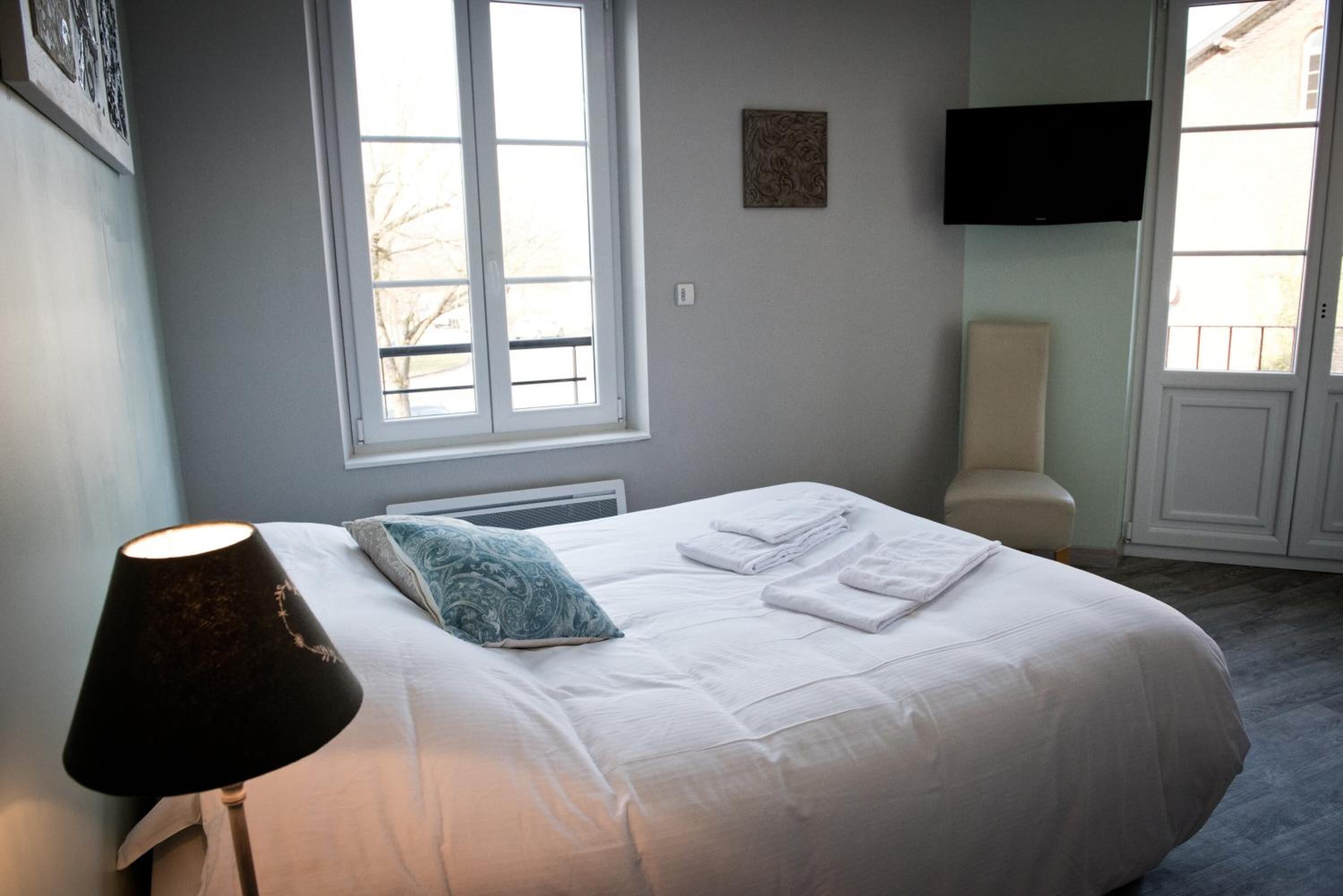 A bedroom with a bed, a window, a wall-mounted TV, and a bedside table.