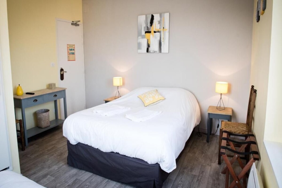 A hotel room with a bed, bedside tables, a chair, and a wall-mounted artwork.