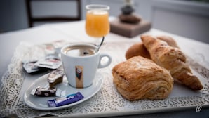 Bandeja de desayuno con cruasanes, una taza de café, un vaso de jugo de naranja y algunas barras de chocolate sobre un mantel de encaje.