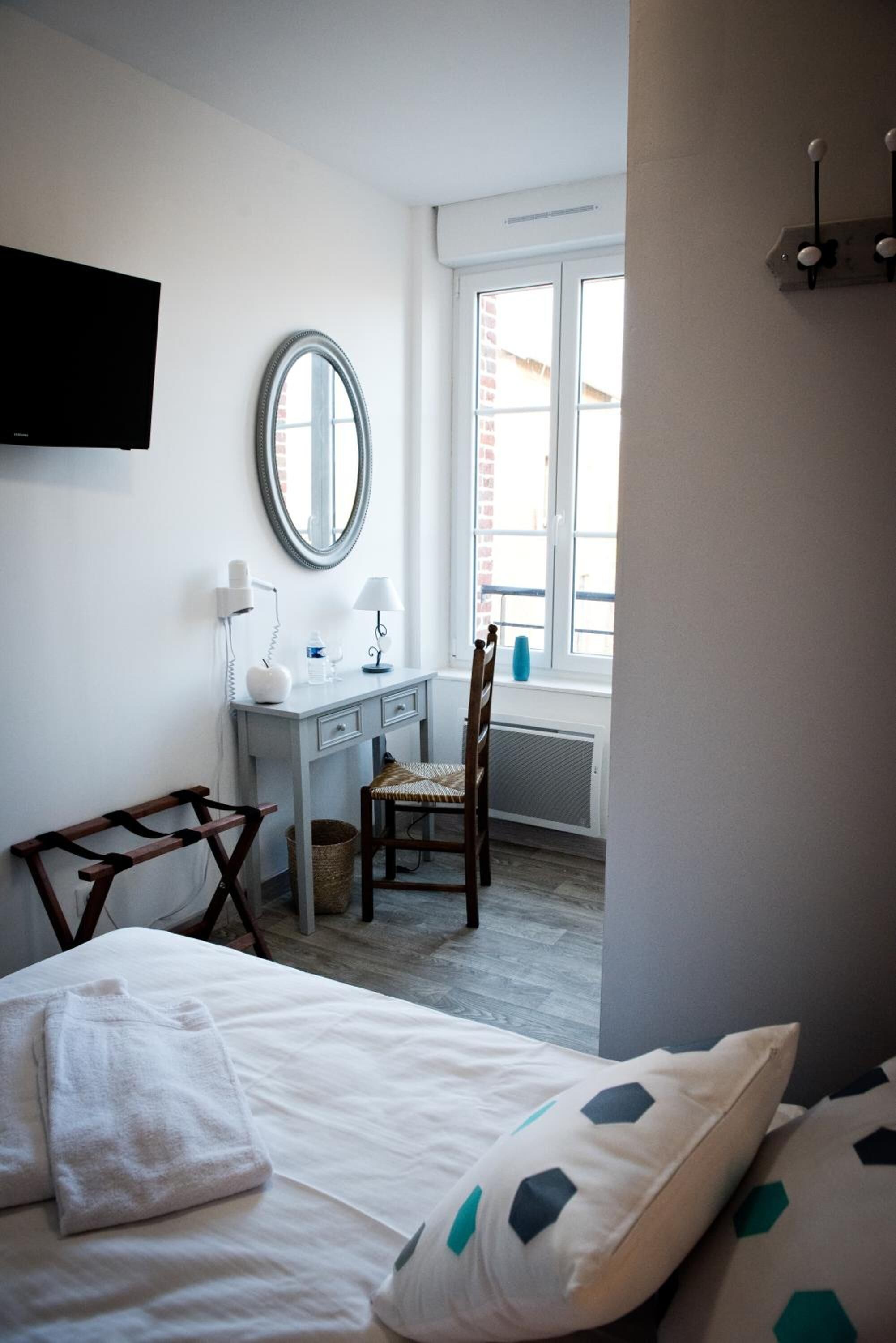 Un dormitorio con cama, escritorio, silla, espejo y ventana.