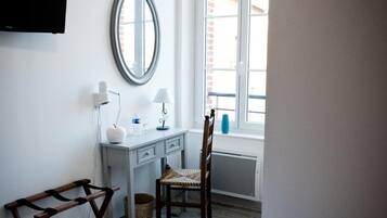 Un dormitorio con cama, escritorio, silla, espejo y ventana.