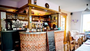 Zona de bar con mostrador de ladrillo, estantes con botellas y copas, una cafetera y un menú en una pizarra.