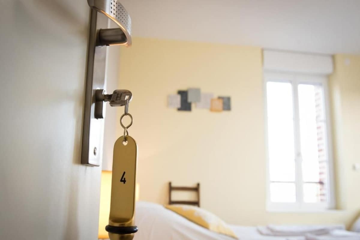 Habitación de hotel con cama, portal para tarjetas llave en la pared y ventana con persianas.