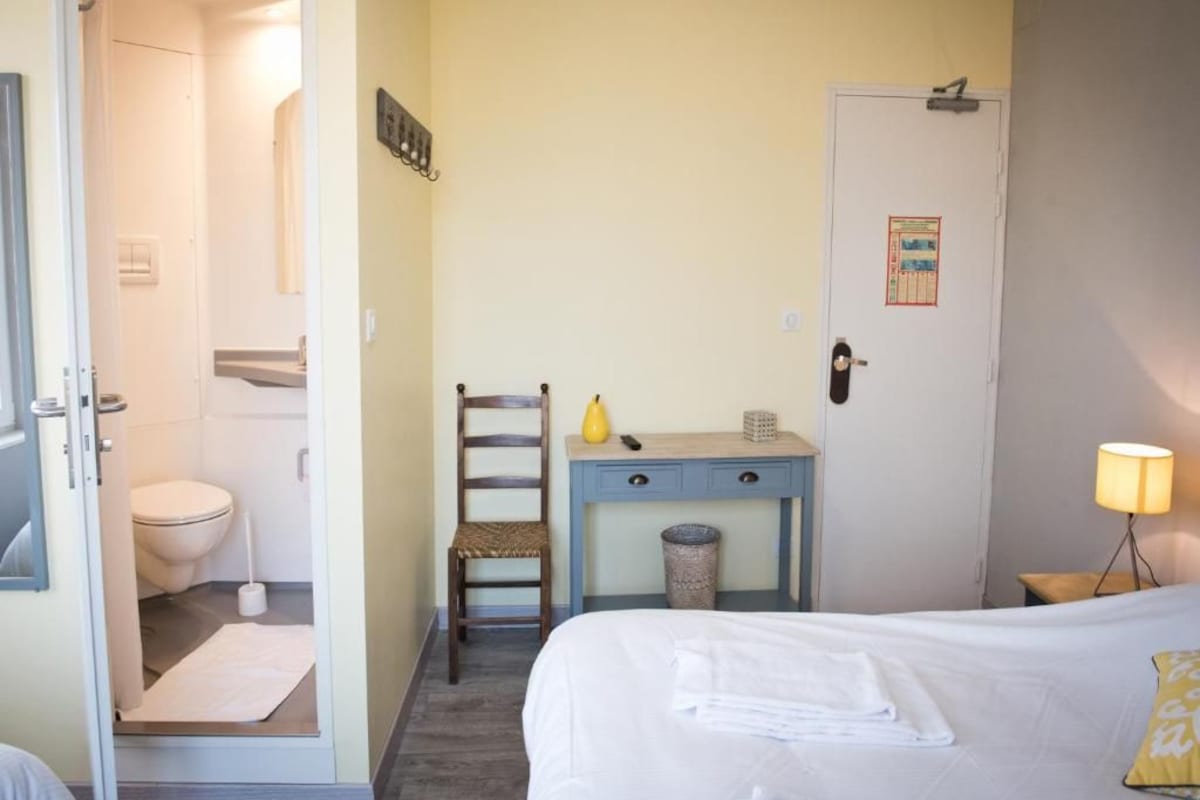 A hotel room with a bed, a desk with a chair, a toilet, and a door.