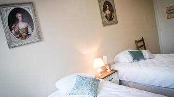 A bedroom with two beds, a nightstand with a lamp, and two framed portraits on the wall.