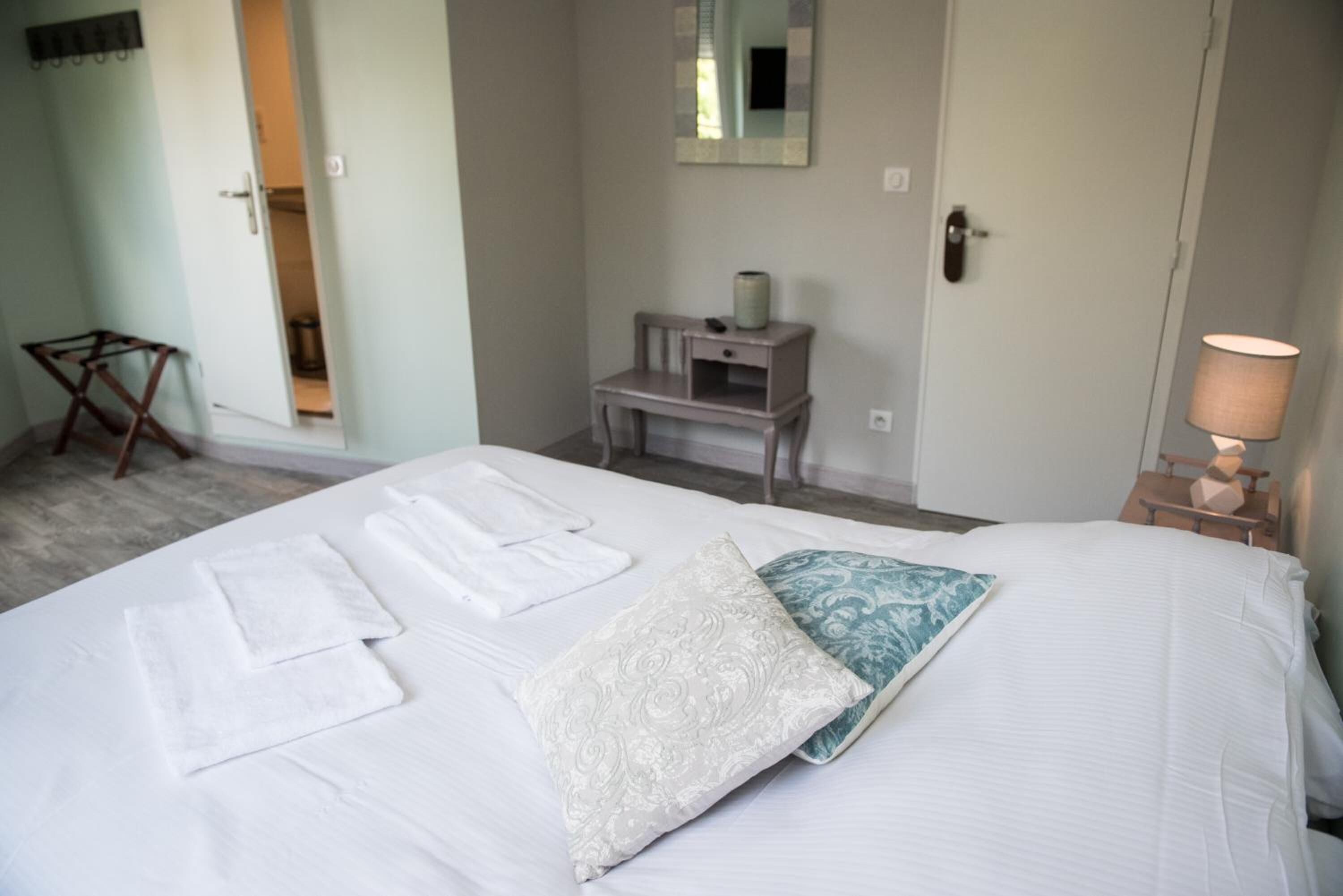 Ein Hotelzimmer mit einem Bett, einem Nachttisch mit Lampe, einem Spiegel an der Wand und einem kleinen Schreibtisch mit Stuhl.