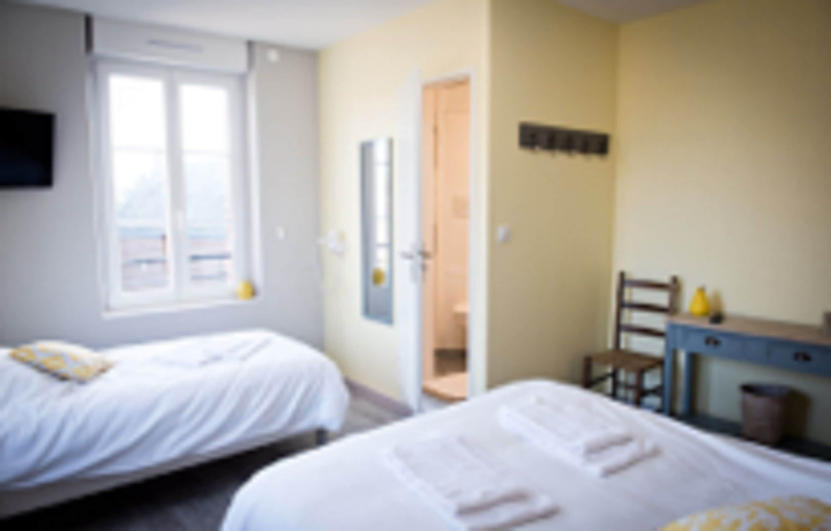 Quarto com duas camas, uma escrivaninha e uma cadeira.