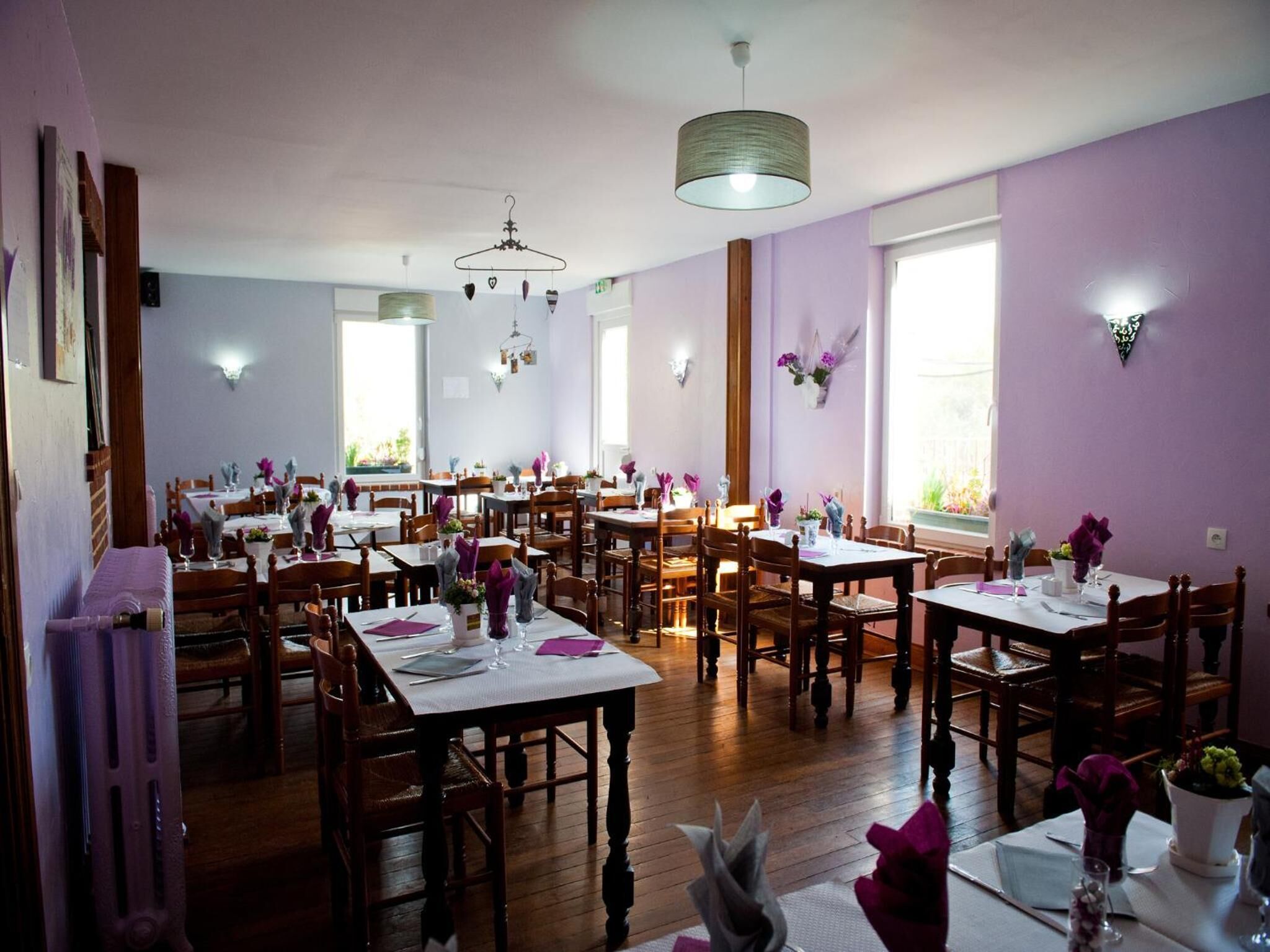 A dining area with multiple tables and chairs, wooden floors, and pendant lighting.
