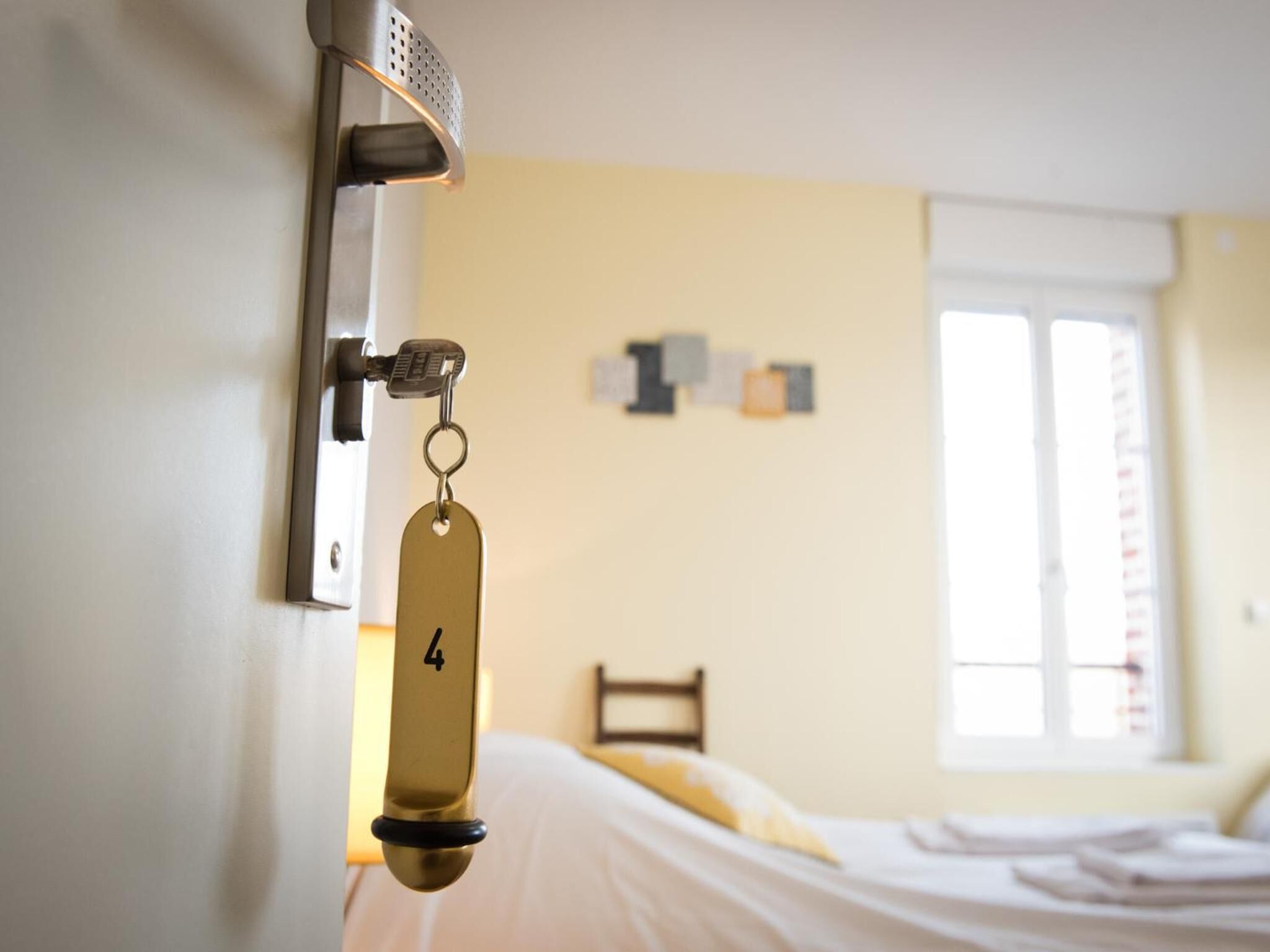 A hotel room with a bed, a wall-mounted key lock, and a window with blinds.