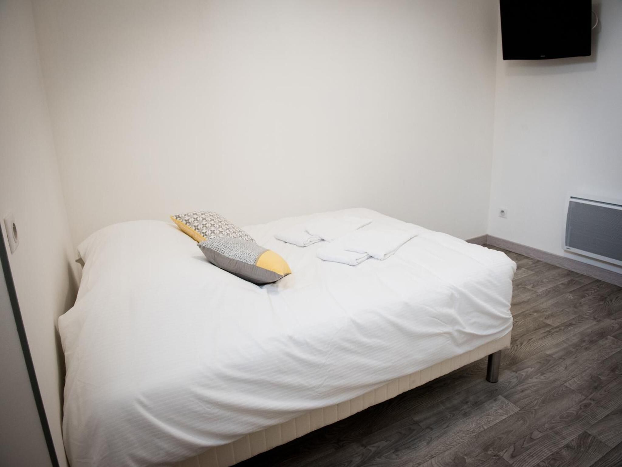 A single bed with a white mattress and a patterned pillow, a folded white towel, and a wall-mounted air conditioning unit.