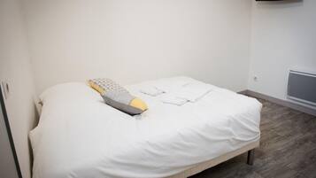 A single bed with a white mattress and a patterned pillow, a folded white towel, and a wall-mounted air conditioning unit.