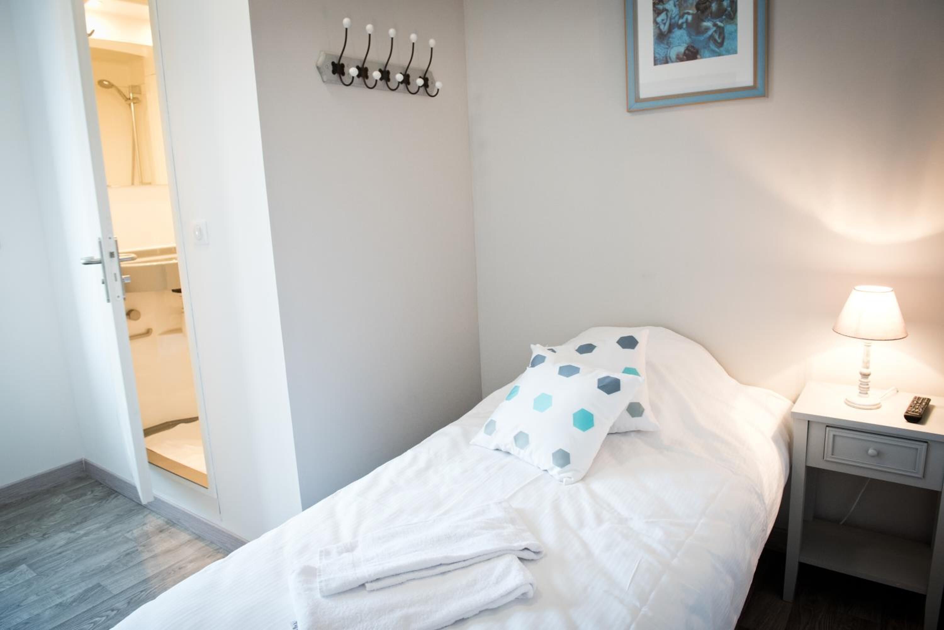 A neatly made bed with white bedding and a polka dot pillow, a bedside lamp, a small bedside table with a remote control, and a wall-mounted light fixture.