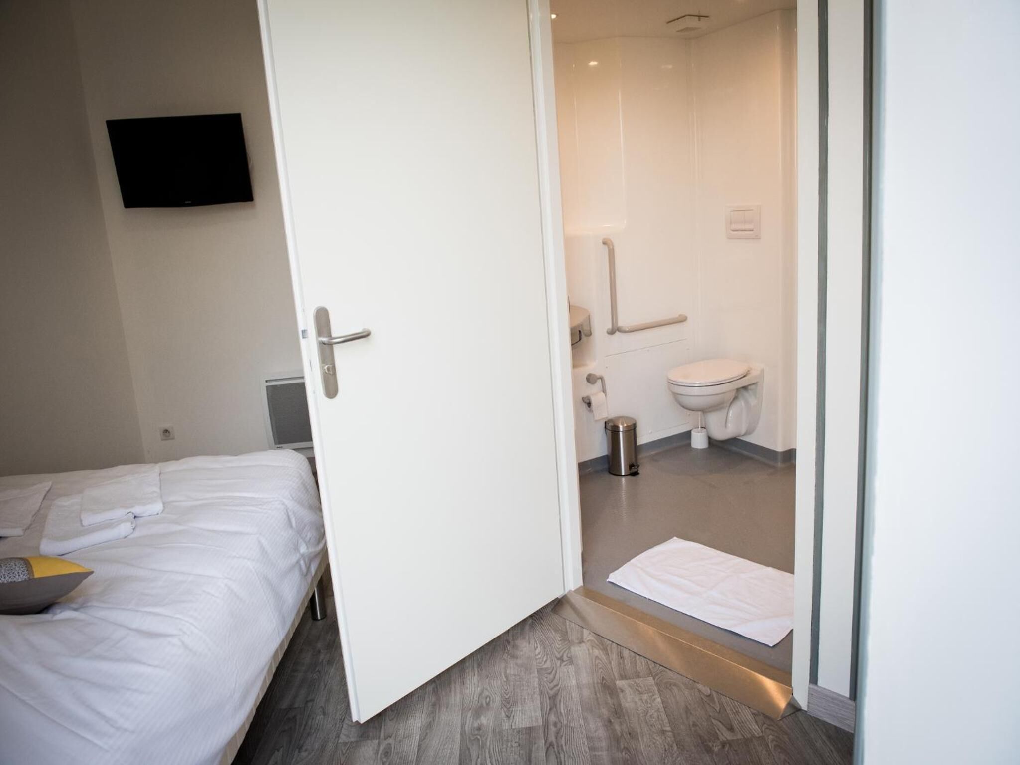 Een hotelkamer met een bed, een witte deur naar een badkamer met toilet en douche.