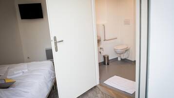 Een hotelkamer met een bed, een witte deur naar een badkamer met toilet en douche.