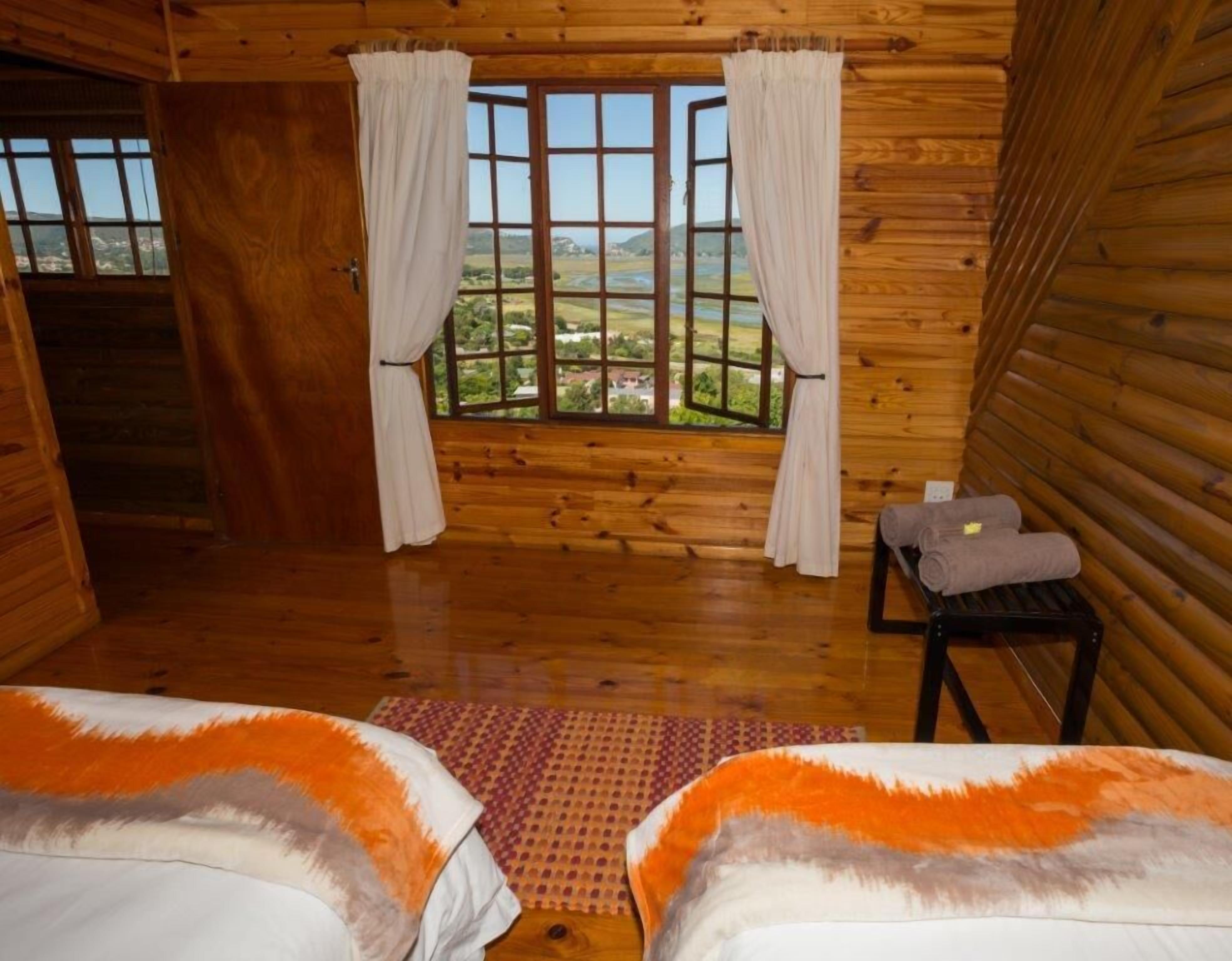 A cabin room with two beds, a window with curtains, a small table with towels, and a view of a landscape.
