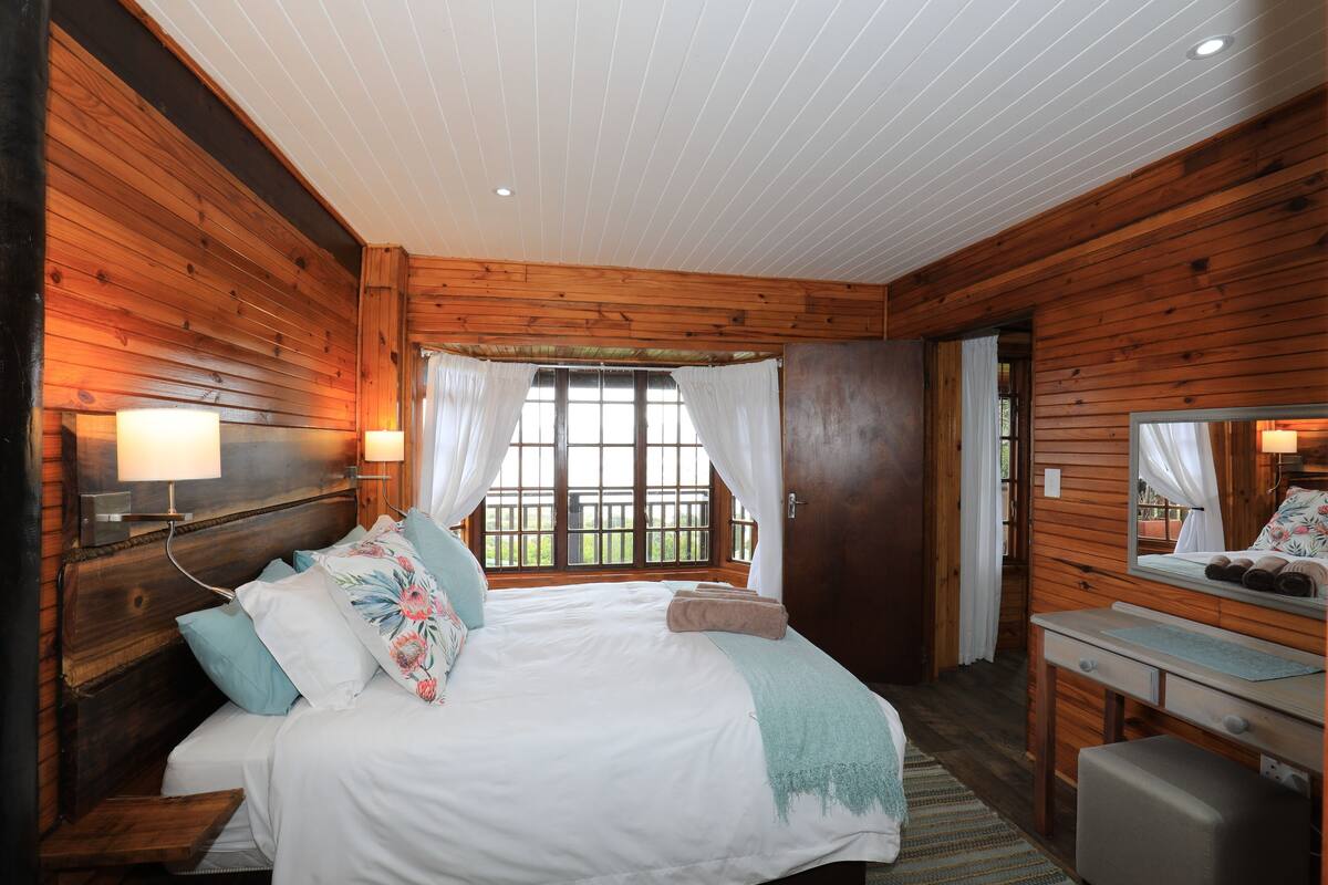 A wooden cabin bedroom with a bed, bedside table, and a window with curtains.