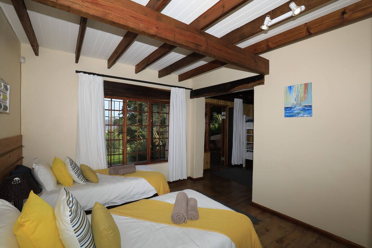 A room with two beds, wooden beams, a window with curtains, and a painting on the wall.