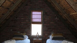 Een kamer met twee bedden, een raam met jaloezieën en een houten plafond.
