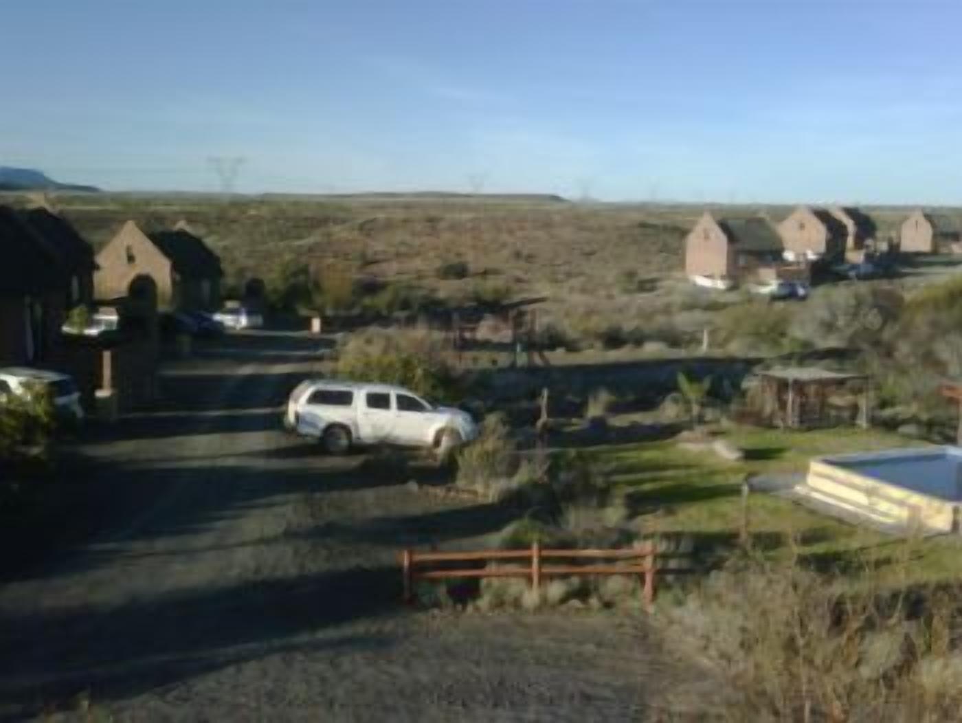 Una zona rural con varias construcciones pequeñas de una sola planta y techos a dos aguas, probablemente casas de huéspedes o cabañas, alineadas a lo largo de un camino de tierra.