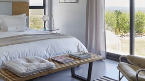 A modern bedroom with a large bed, a bedside table with a lamp, a chair, and a view of the outdoors. - HaesFarm (Stanford)