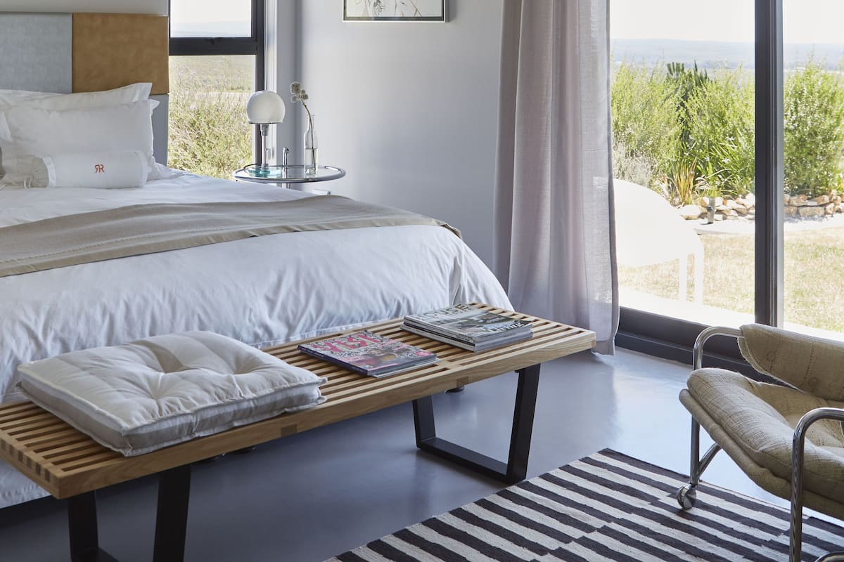 Un dormitorio moderno con una cama grande, una mesita de noche con lámpara, una silla y vistas al exterior.