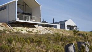 A modern house with a large balcony, situated on a grassy hill. - HaesFarm (Stanford)