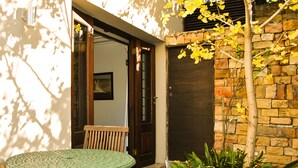 A patio with a round table and chairs, a wooden bench, and a stone wall with a tree. - Wessels House Studio (Cape Town)