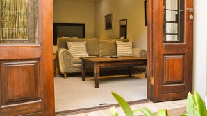 A living room with a wooden coffee table, a sofa with striped cushions, and a large window with a view of bamboo. - Wessels House Studio (Cape Town)
