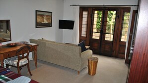 A room with a sofa, a wooden table, a television, and a door with a view of greenery outside. - Wessels House Studio (Cape Town)