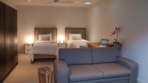A hotel room with two beds, a grey sofa, a wooden stool, a laptop on a side table, and a potted orchid. - Wessels House Studio (Cape Town)