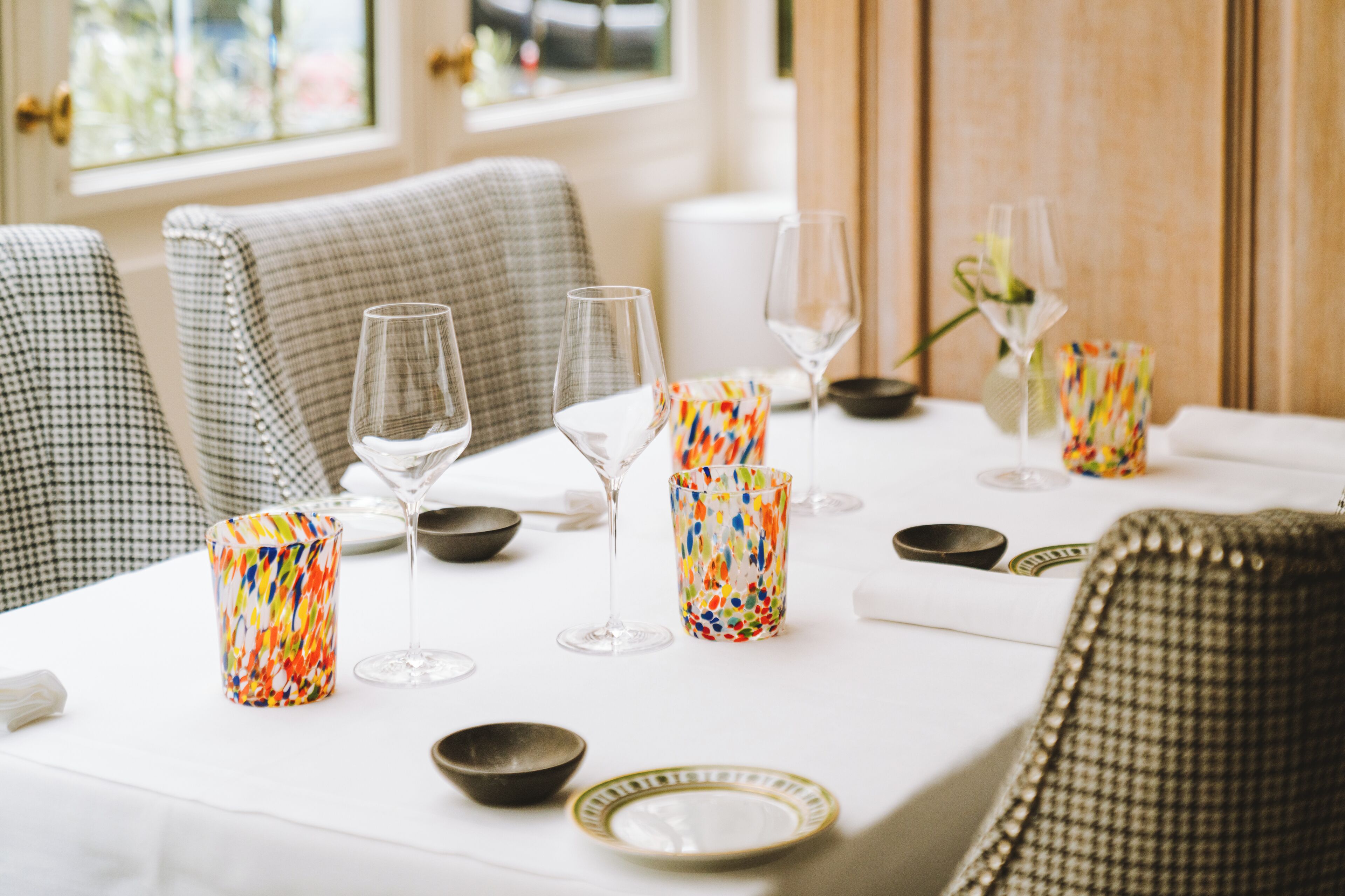 A dining table set with glassware, colorful candle holders, and a white tablecloth.