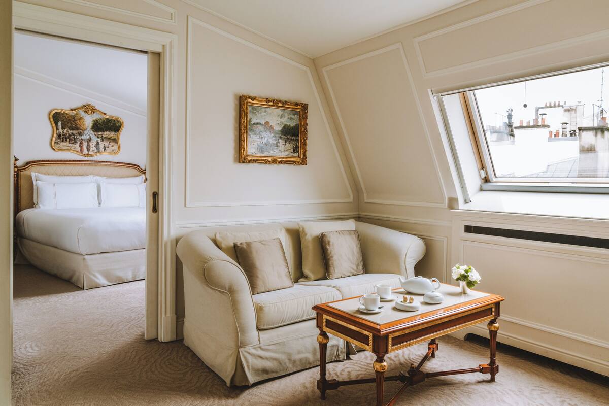 A room with a bed, a sofa, a table with cups and a vase, and a painting on the wall.