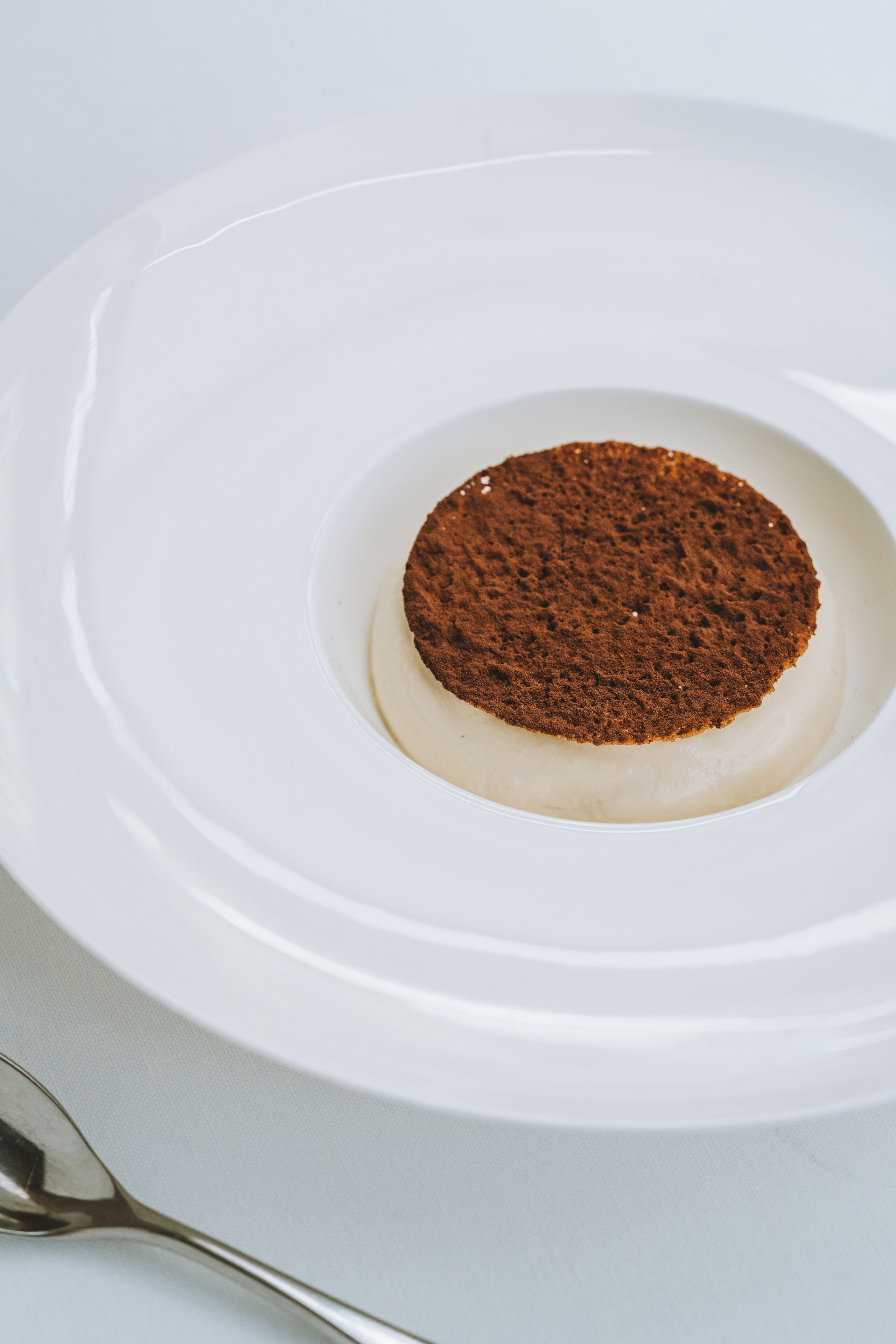 A white plate with a dessert featuring a circular brown topping.