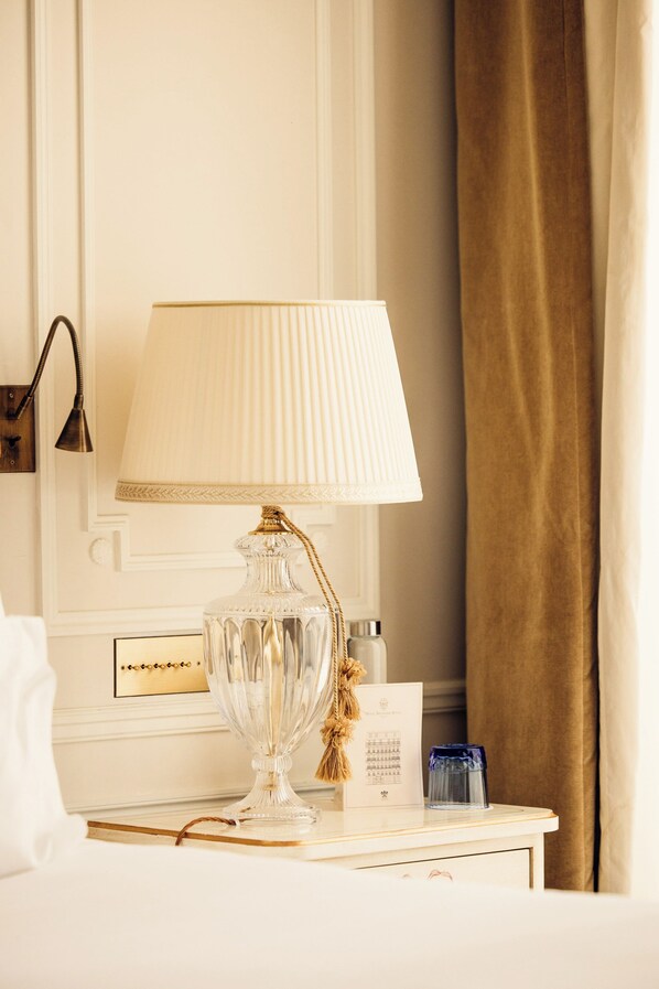 A neatly arranged hotel room with a bedside table featuring a clear glass lamp, a small blue container, and a framed certificate. - Hôtel Splendide Royal Paris - Relais & Châteaux (Paris)