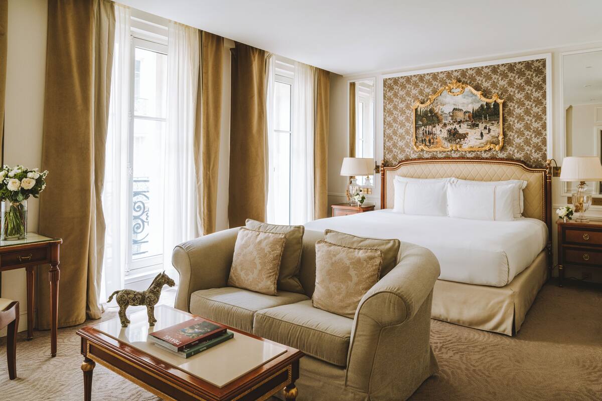 A hotel room with a large bed, a sofa, a small table with books, and a decorative horse statue.