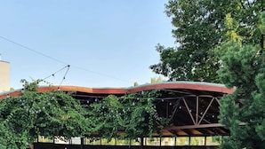 Un espace extérieur aménagé en terrasse, avec des meubles en osier, un sol en pierre et un coin salon couvert doté d’un toit rouge.