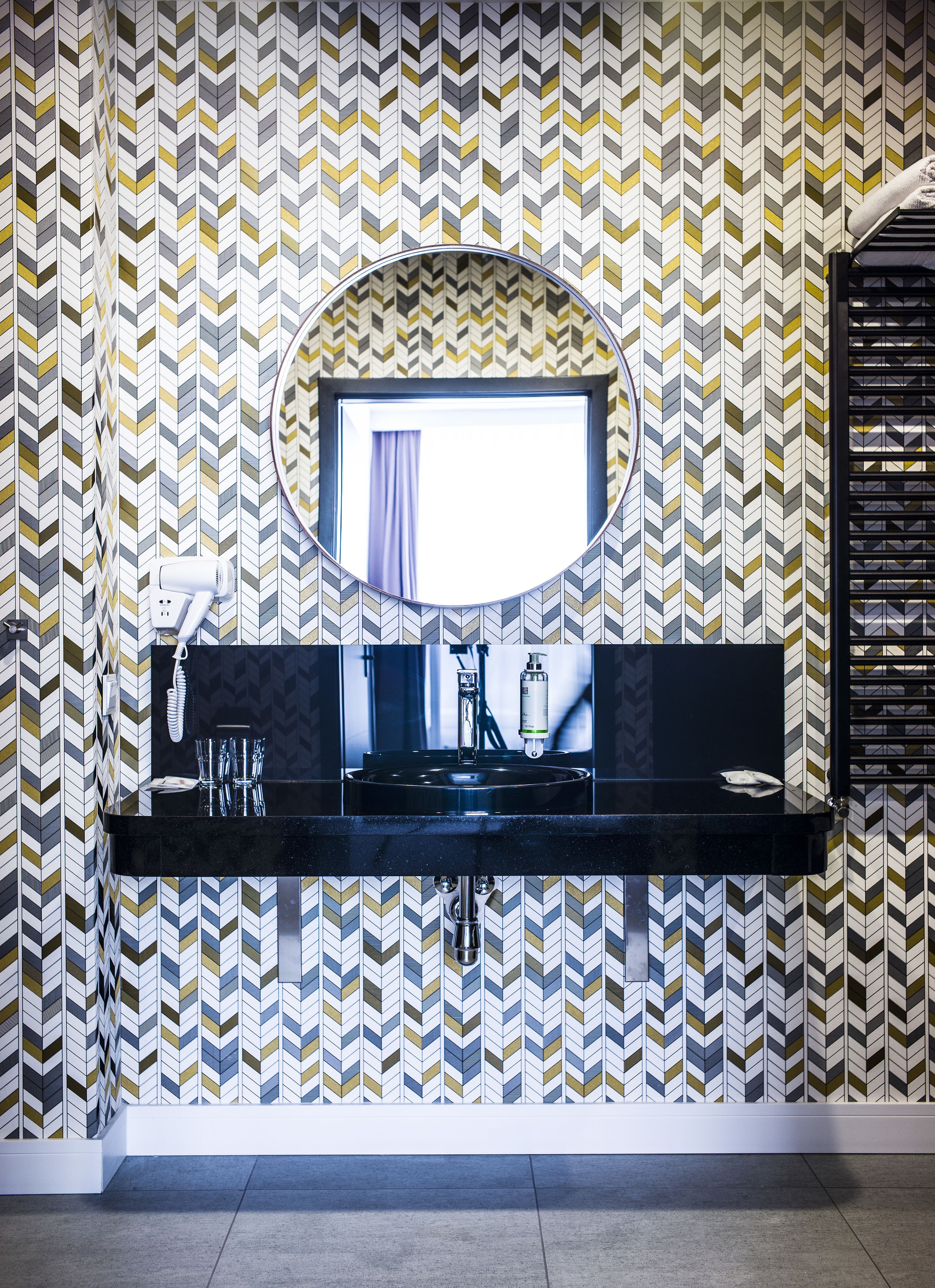A modern bathroom with a black vanity, a mirror, and a patterned wall.