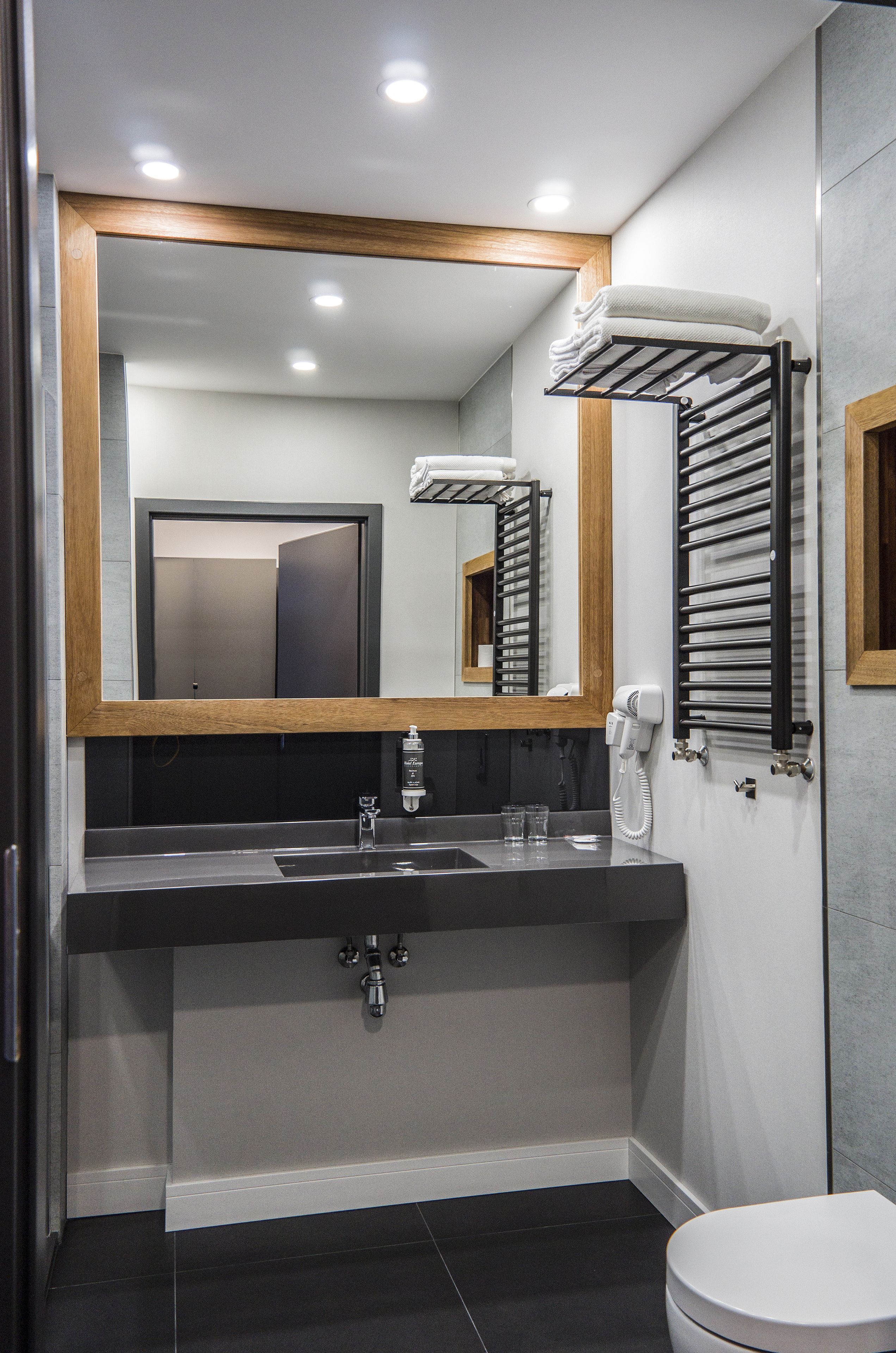 Une salle de bain moderne avec un grand miroir, un lavabo avec un robinet, des toilettes et un porte-serviettes.