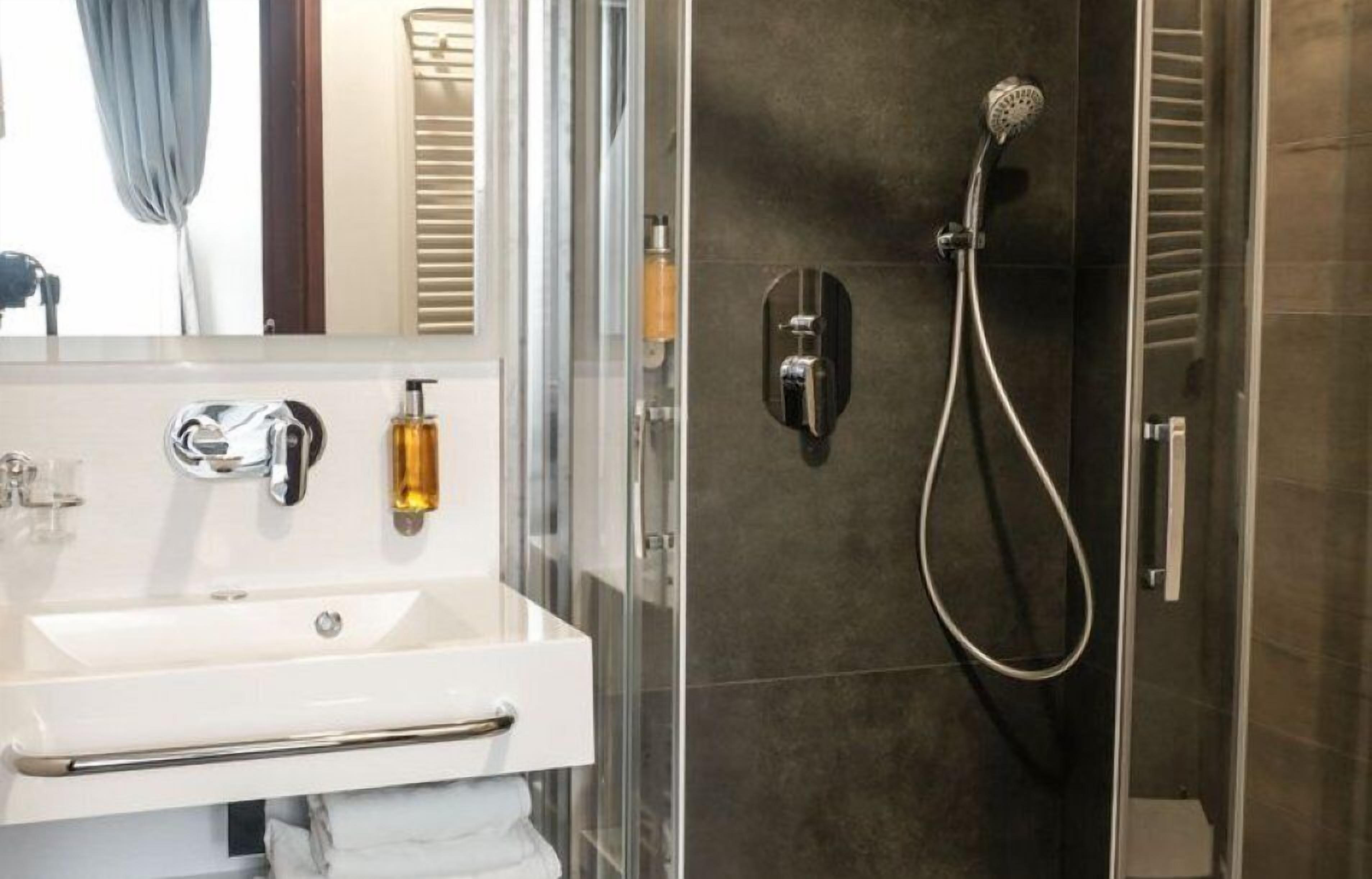 Ein Badezimmer mit weißem Waschbecken, einer Duschkabine aus Glas und einer dunkel gefliesten Wand.
