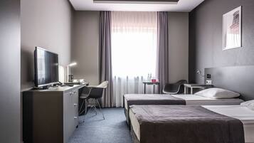 Quarto de hotel com cama, escrivaninha com computador, cadeira e televisão.